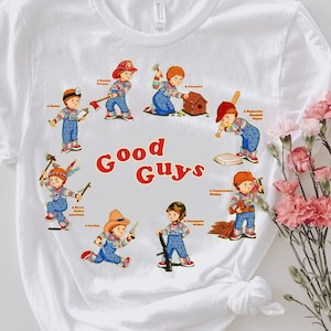 May include: White t-shirt with a graphic of a group of children dressed as different professions. The text "Good Guys" is printed in red and orange letters.