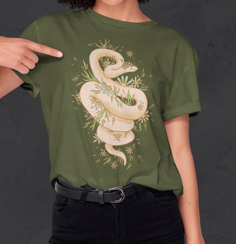 May include: A green t-shirt with a white snake wrapped around a cluster of white and yellow flowers. The snake is curled up and has a crown of flowers on its head.