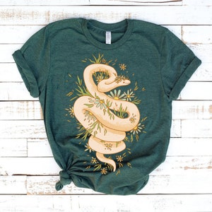 May include: A green t-shirt with a white snake wrapped around a cluster of yellow and white flowers. The snake is curled up and has a floral pattern on its body.