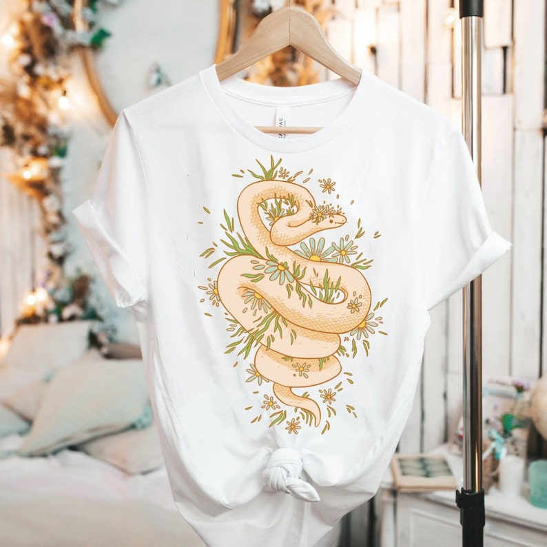 May include: White t-shirt with a graphic of a snake wrapped in flowers. The snake is light beige and the flowers are white and green.