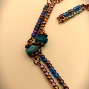 Może przedstawiać: Wielorzędowy naszyjnik z miedzianym drutem i niebieskimi, zielonymi i tęczowymi koralikami. Naszyjnik zawiera turkusowy kamień i niebieską szklaną koralik.