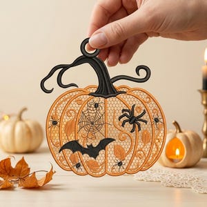 May include: An orange and black pumpkin-shaped ornament featuring intricate lace-like embroidery. The design includes black stitched details of a bat, several spiders, a spiderweb, and leaf patterns, with a black stem and a circular hanging loop.