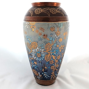 May include: A decorative vase with a copper rim and base, featuring a gradient of blue and teal with gold floral patterns. The upper portion is dark brown with gold floral accents. The vase has a wide body and a narrow neck.