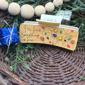May include: A wooden desk organizer with the phrase "I'm fine, everything is fine..." and colorful string lights. A small blue gift box with silver string is to the left. The organizer is set in a woven basket with wooden beads and greenery.