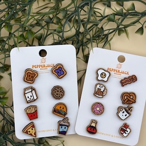 May include: Two white cards with wooden food-themed pins. One card features a bear, toast, milk, fries, pizza, cookie, burger, and a drink. The other card has an egg, bacon, beer, pretzel, donut, coffee, and a dessert.
