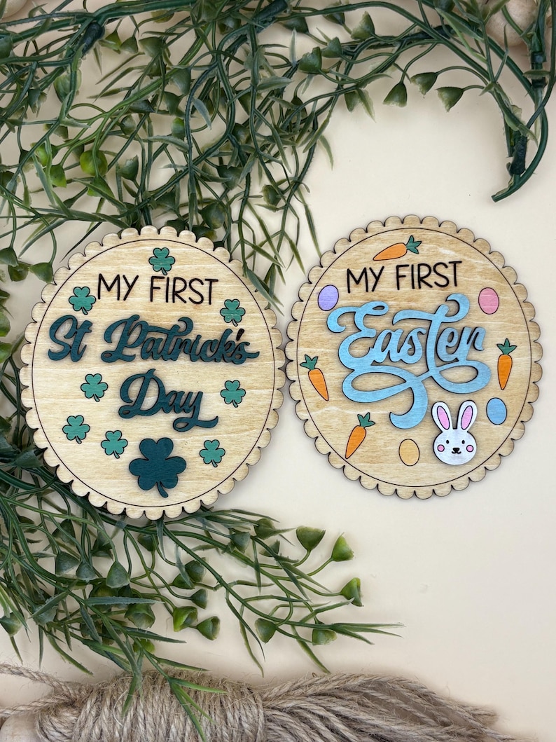 May include: Two wooden round decorations with scalloped edges. One says "My First St. Patrick's Day" with shamrocks. The other says "My First Easter" with carrots, eggs, and a bunny. Both are light brown with green and blue accents.