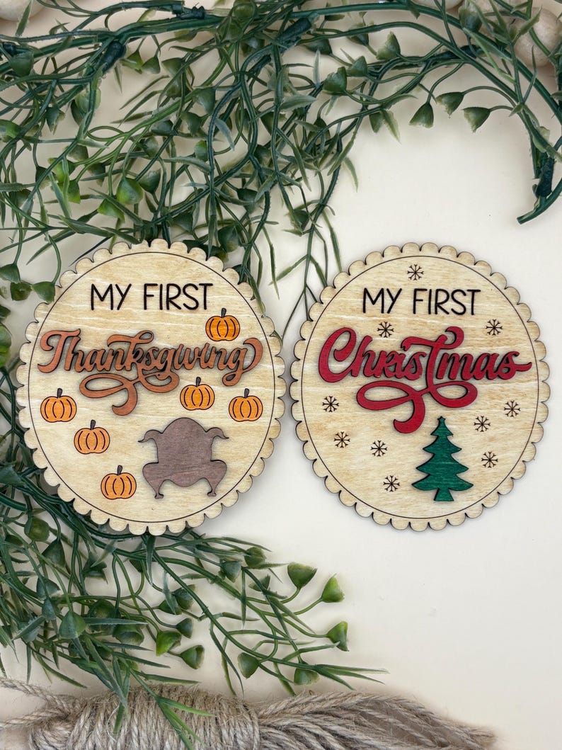 May include: Two wooden round ornaments with scalloped edges. One says "MY FIRST Thanksgiving" with pumpkins and a turkey. The other says "MY FIRST Christmas" with snowflakes and a Christmas tree.