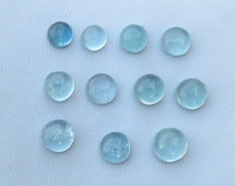 May include: A collection of eleven round, smooth, light blue cabochons arranged in three rows. Each piece features a translucent, polished surface with a domed top, reflecting light evenly across the circular shapes against a plain background.