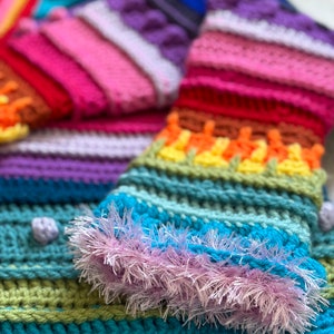 Puede incluir: Una bufanda de crochet colorida con un patr&oacute;n de arco&iacute;ris y un borde esponjoso azul y morado.