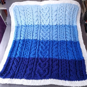 May include: A blue and white knitted blanket with a cable knit pattern. The blanket is made of thick yarn and has a soft, fluffy texture.