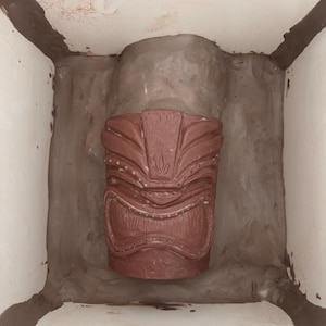 K&ouml;nnte beinhalten: Eine rotbraune Tiki-Statue mit geschnitzten Details, platziert in einem hellen, geschlossenen Raum. Die Statue zeigt ein stilisiertes Gesicht und geometrische Muster, die ein polynesischen Thema hervorrufen.