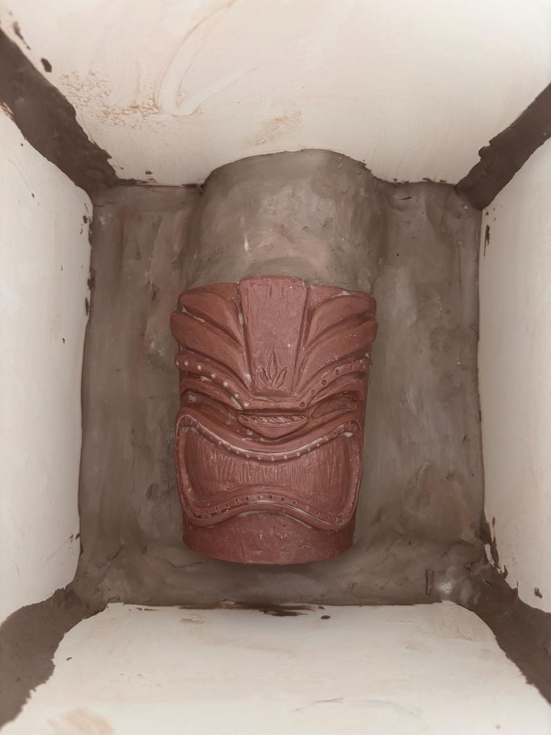 K&ouml;nnte beinhalten: Eine rotbraune Tiki-Statue mit geschnitzten Details, platziert in einem hellen, geschlossenen Raum. Die Statue zeigt ein stilisiertes Gesicht und geometrische Muster, die ein polynesischen Thema hervorrufen.