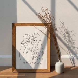 K&ouml;nnte beinhalten: Ein gerahmtes Strichbild von zwei Frauen, Sophia und Chloe, mit einer einfachen schwarzen Umrandung auf wei&szlig;em Hintergrund. Der Rahmen ist aus hellbraunem Holz.