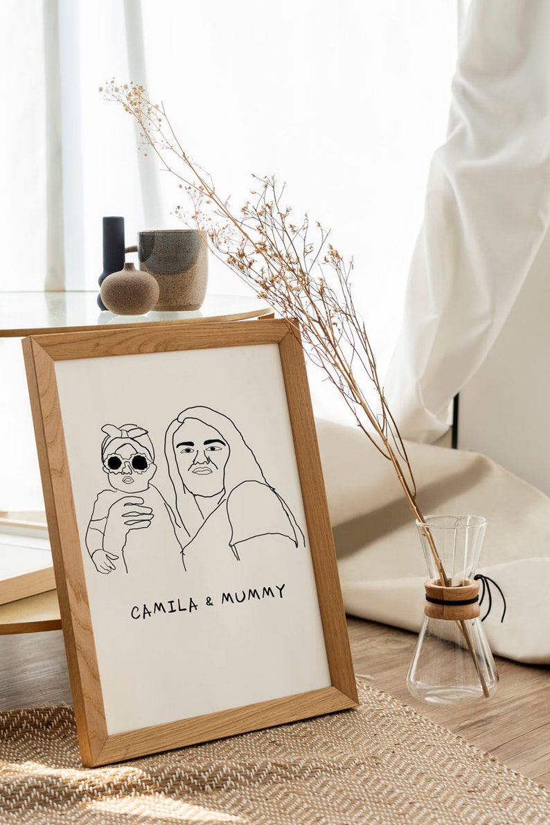 K&ouml;nnte beinhalten: Ein gerahmtes Schwarzwei&szlig;-Strichbild einer Mutter und ihrer Tochter. Die Mutter h&auml;lt die Tochter in ihren Armen. Der Text "CAMILLA & MUMMY" steht unter der Zeichnung.