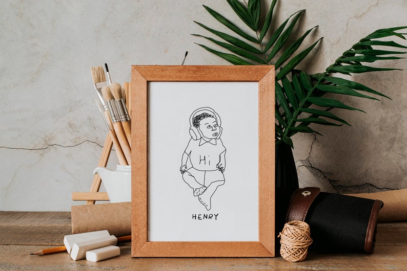K&ouml;nnte beinhalten: Eine gerahmte Schwarzwei&szlig;-Zeichnung eines Babys mit Kopfh&ouml;rern und einem Shirt mit der Aufschrift "Hi". Der Name des Babys, "HENRY", steht unter der Zeichnung.