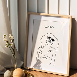 K&ouml;nnte beinhalten: Ein gerahmtes Schwarzwei&szlig;-Strichbild einer Frau mit Sonnenbrille mit dem Text "Lauren" und "Loel!" auf wei&szlig;em Hintergrund.