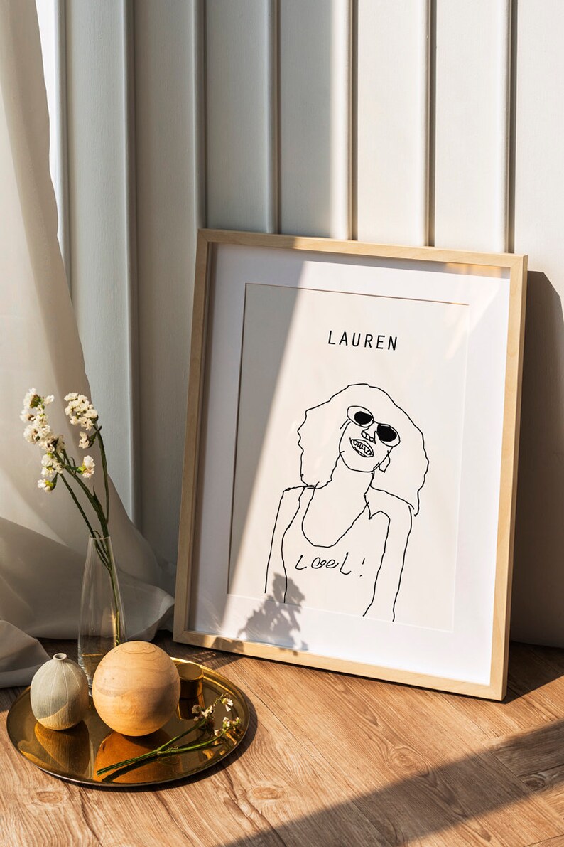K&ouml;nnte beinhalten: Ein gerahmtes Schwarzwei&szlig;-Strichbild einer Frau mit Sonnenbrille mit dem Text "Lauren" und "Loel!" auf wei&szlig;em Hintergrund.