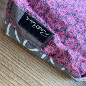 Puede incluir: Una bolsa de tela rosa y gris con una etiqueta negra que dice "Pink & Proud".