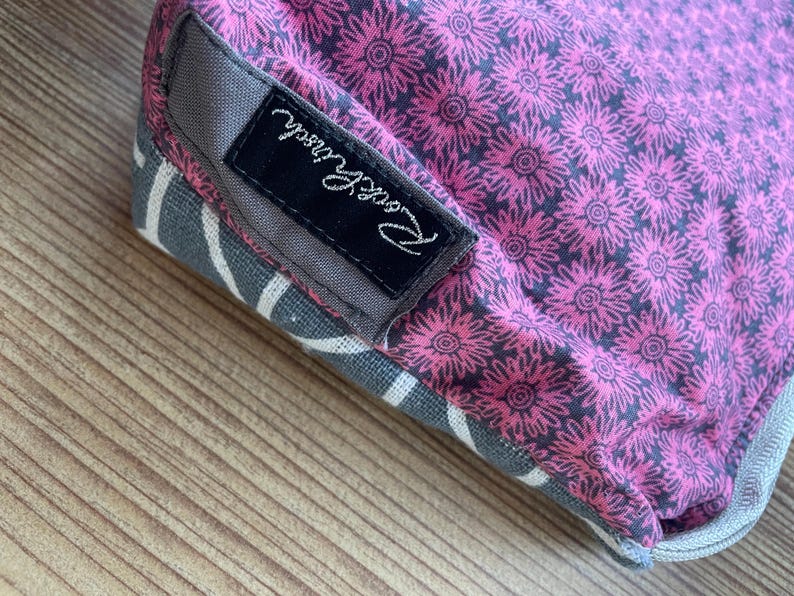 Puede incluir: Una bolsa de tela rosa y gris con una etiqueta negra que dice "Pink & Proud".