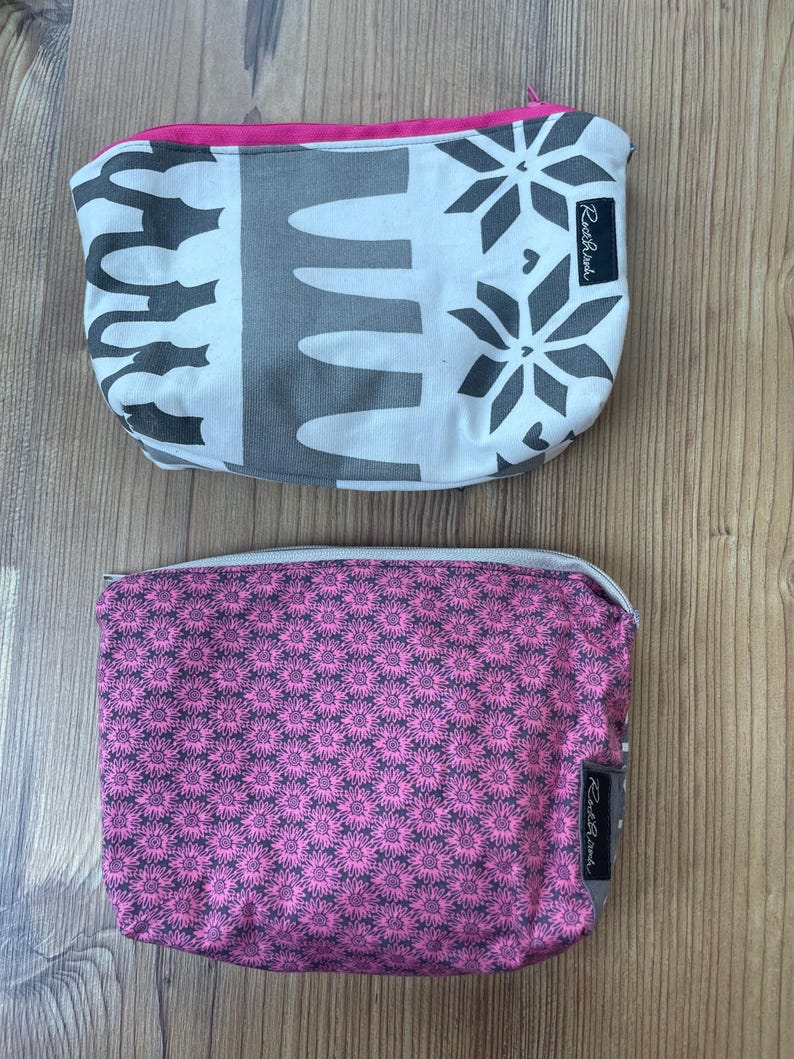 Puede incluir: Dos estuches con cremallera con diferentes patrones. El estuche superior es blanco con dise&ntilde;os geom&eacute;tricos negros y una cremallera rosa. El estuche inferior es rosa con un patr&oacute;n floral negro. Ambos estuches tienen una etiqueta negra con el texto "Rooster & Hen" en ellos.