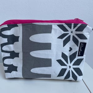 Puede incluir: Una bolsa blanca con cremallera con un patr&oacute;n geom&eacute;trico blanco y negro. La bolsa tiene una cremallera rosa y una etiqueta negra con el texto "Rosa & Black" en ella.