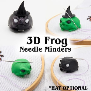 May include: A collection of 3D-printed frog needle minders in black and green, some wearing witch hats. The frogs have white eyes and are designed to hold needles in place during cross-stitch or embroidery projects. Text on the image reads "3D Frog Needle Minders" and "*HAT OPTIONAL."