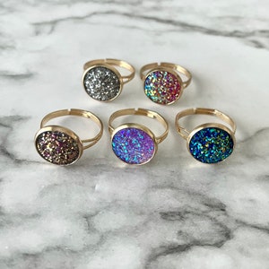 May include: Five gold rings with round, sparkly, colorful stones. The stones are silver, pink, purple, green, and brown.