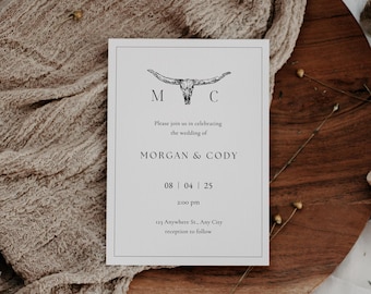 May include: A white wedding invitation with a black and white illustration of a bull skull with the letters M and C on either side. The text reads "Please join us in celebrating the wedding of Morgan & Cody 08 | 04 | 25 2:00 pm 123 Anywhere St., Any City reception to follow"