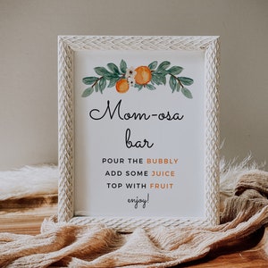 May include: White sign with a floral design and the text "Mom-osa bar" with instructions to "Pour the bubbly, add some juice, top with fruit, enjoy!"