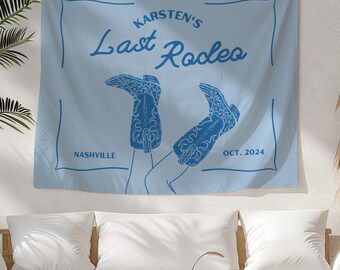 May include: A light blue tapestry with the text "Karsten's Last Rodeo" in a white box. The text "Nashville" is in the lower left corner and "Oct. 2024" is in the lower right corner. The tapestry features a pair of blue cowboy boots with the tops of the boots facing up.