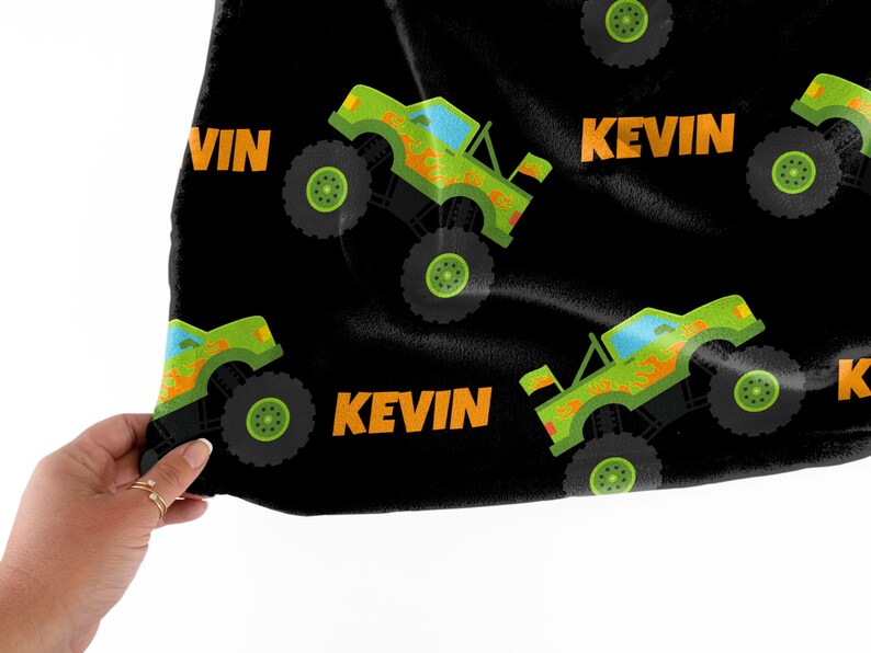 Może przedstawiać: Czarny materiał z powtarzającym się wzorem zielonych monster truck&oacute;w z pomarańczowymi płomieniami i nazwą "Kevin" w pomarańczowym tekście.