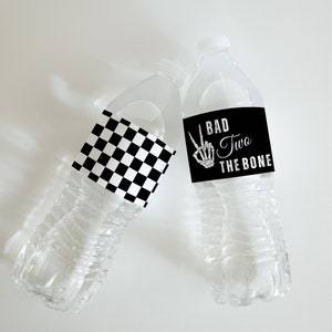 May include: Two water bottles with labels. One bottle has a black and white checkered label. The other bottle has a black label with a skeleton hand making a peace sign and the text "Bad Two The Bone".