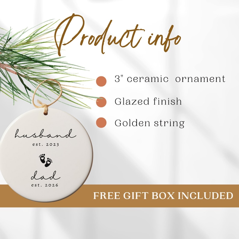 May include: A white ceramic ornament with the words "husband est. 2023" and "dad est. 2026" printed in black. The ornament has a glazed finish and a golden string for hanging. The product info states it is a 3-inch ornament.