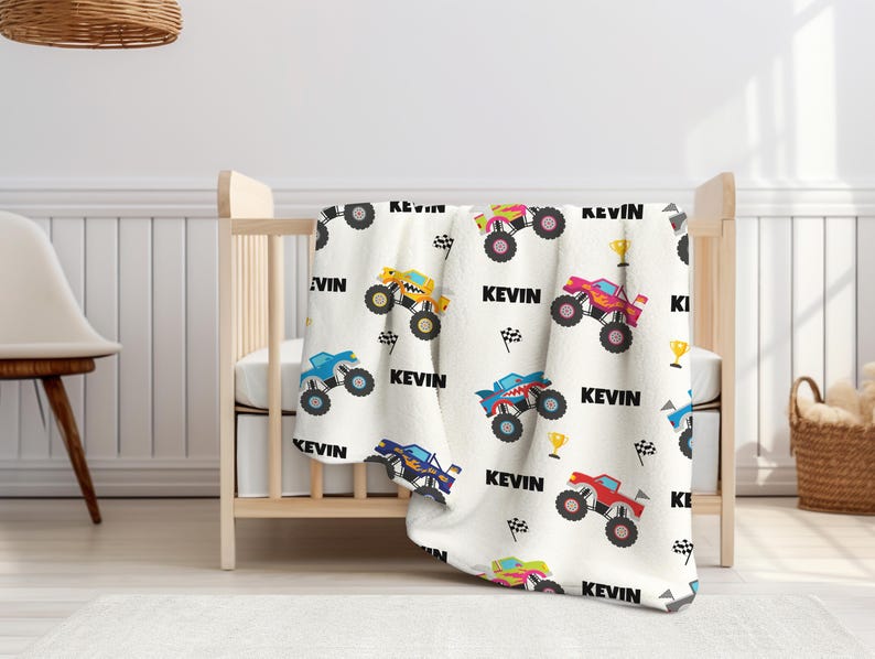 May include: White baby blanket with a repeating pattern of monster trucks in various colors, including blue, yellow, red, and pink. The blanket features the name "Kevin" repeated throughout the design.