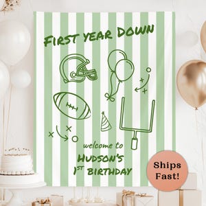 May include: A rectangular fabric backdrop featuring vertical sage green and white stripes. The text reads FIRST YEAR DOWN and welcome to HUDSON'S 1ST BIRTHDAY. Graphics include a football helmet, a football, balloons, a party hat, and goal posts.