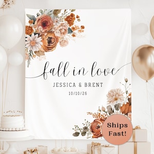May include: A white fabric backdrop featuring a floral arrangement of rust, orange, and cream flowers in the top left and bottom right corners. The text reads fall in love, JESSICA & BRENT, and 10/10/26 in black script and sans-serif fonts.