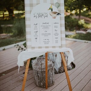 May include: A brown and white gingham sign with a duck illustration and the text "CARSON my first year". The sign lists the child's height, weight, and other milestones, including favourite foods, nicknames, and toys.