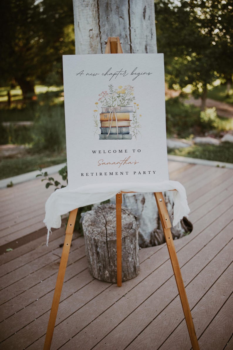 May include: A white sign with the text "A new chapter begins" and a watercolour illustration of a stack of books with flowers on top. The sign also says "Welcome to Samantha's Retirement Party". The sign is on a wooden easel.