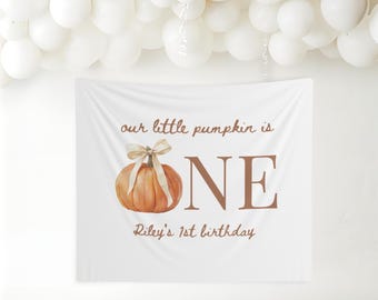 Può includere: Banner bianco con la scritta "our little pumpkin is ONE" e "Riley's 1st birthday". Il banner presenta una zucca ad acquerello con un fiocco. Palloncini bianchi sullo sfondo.