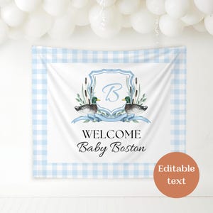 May include: A blue and white gingham backdrop with a white banner featuring a crest with the letter "B" and two ducks. The banner reads "Welcome Baby Boston" and has editable text.