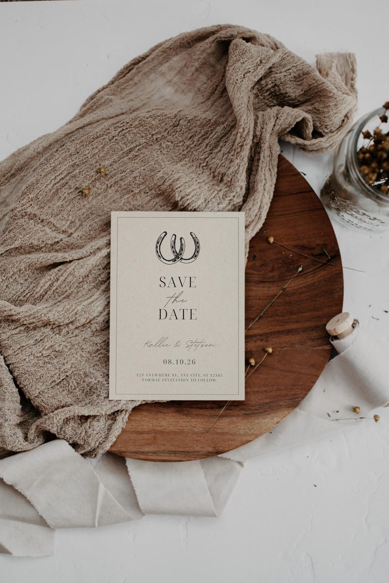 K&ouml;nnte beinhalten: Eine rustikale Save-the-Date-Karte mit braunem Hintergrund und schwarzem Text. Die Karte zeigt zwei Hufeisen und den Text "Save the Date" mit den Namen "Kalie & Steffen" und dem Datum "08.10.26".