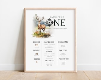 May include: A printable first birthday chart for a boy named Carson. The chart features a watercolor illustration of a deer in a forest setting. It includes details like height, weight, favorite foods, nickname, favorite toys, and favorite songs. The chart is decorated with a green target and the number "ONE" in a bold font.