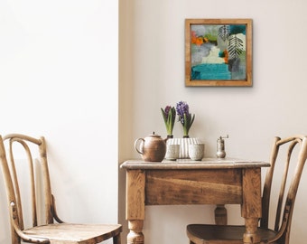 May include: A wooden table with two chairs, a teapot, and two small plants with purple flowers. A framed abstract painting with green, blue, and orange colors hangs on the wall behind the table.
