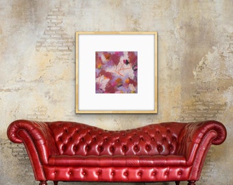 May include: A red leather tufted sofa sits in front of a wall with a framed abstract painting. The painting features pink, purple, and orange hues with white brushstrokes.