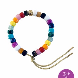 May include: A colorful beaded bracelet with a gold charm and a gold cord closure. The beads are made of various materials, including gemstones and glass. The bracelet is tied with a gold cord and has a small gold charm.