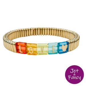 Peut inclure: Un bracelet extensible en or avec des perles colorées qui épellent le mot "LOVE". Les perles sont rouges, orange, jaunes, vertes, bleues et bleu clair. La dernière perle est en forme de cœur.