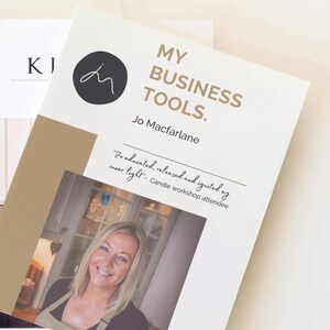 May include: A white book with the title "My Business Tools." by Jo Macfarlane. The book has a brown background with a photo of a woman smiling. The text "Jo educated, released and ignited my inner light." is written in cursive on the book.