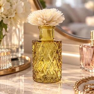 May include: A yellow glass diffuser bottle with a diamond-patterned texture and a narrow neck, topped with a large, cream-coloured, multi-petaled sola wood flower diffuser. The bottle is cylindrical with a flat base and a clear, translucent finish.