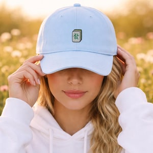 Peut inclure: Casquette de baseball bleu clair avec un motif brodé vert et blanc. La casquette a une visière incurvée et une sangle réglable. Le motif est un caractère chinois. La casquette est en matière souple.