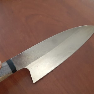 May include: A silver chef's knife with a wooden handle. The knife has a black stripe on the handle.